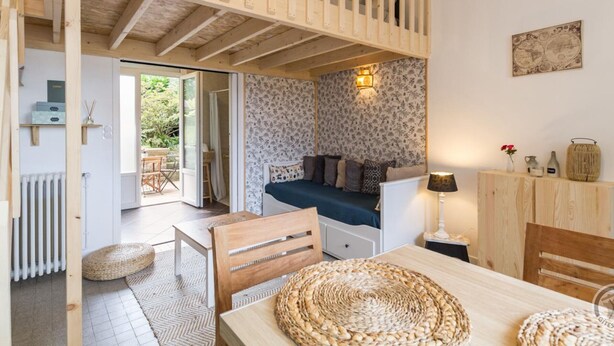 Une pièce chaleureuse avec un plafond en bois, un canapé bleu, une table à manger et une vue sur l’extérieur.