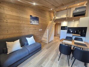 Ein gemütliches Blockhaus-Interieur mit Holzvertäfelung, einer Couch, einem Esstisch mit Stühlen, einer Küchenzeile und einer Treppe.