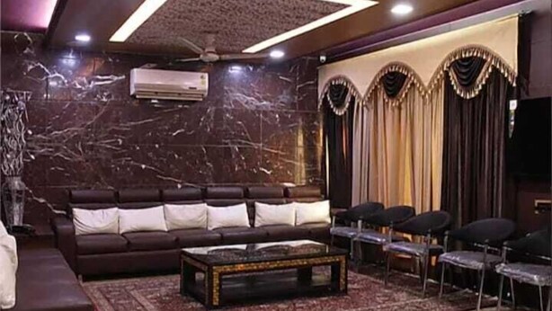 A spacious living room with a dark brown sofa, a coffee table, and a patterned rug. - SR GUEST HOUSE  (Agra)