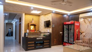 A hotel reception area with a reception desk, a Coca-Cola refrigerator, a sofa, and a ceiling fan. - SR GUEST HOUSE  (Agra)