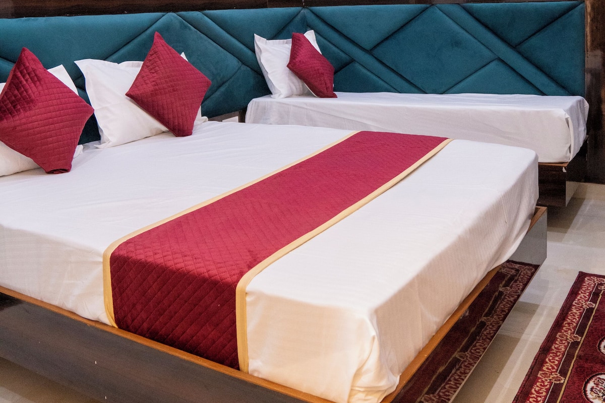 Quarto de hotel com cama grande, duas almofadas, manta vermelha e parede estampada.