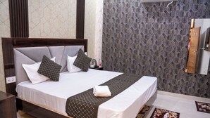 A neatly made bed with a wooden headboard, a nightstand with a bottle and a glass, and a patterned rug on the floor. - SR GUEST HOUSE  (Agra)