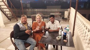 Three people seated at a table on a rooftop terrace with a city view in the background. - SR GUEST HOUSE  (Agra)