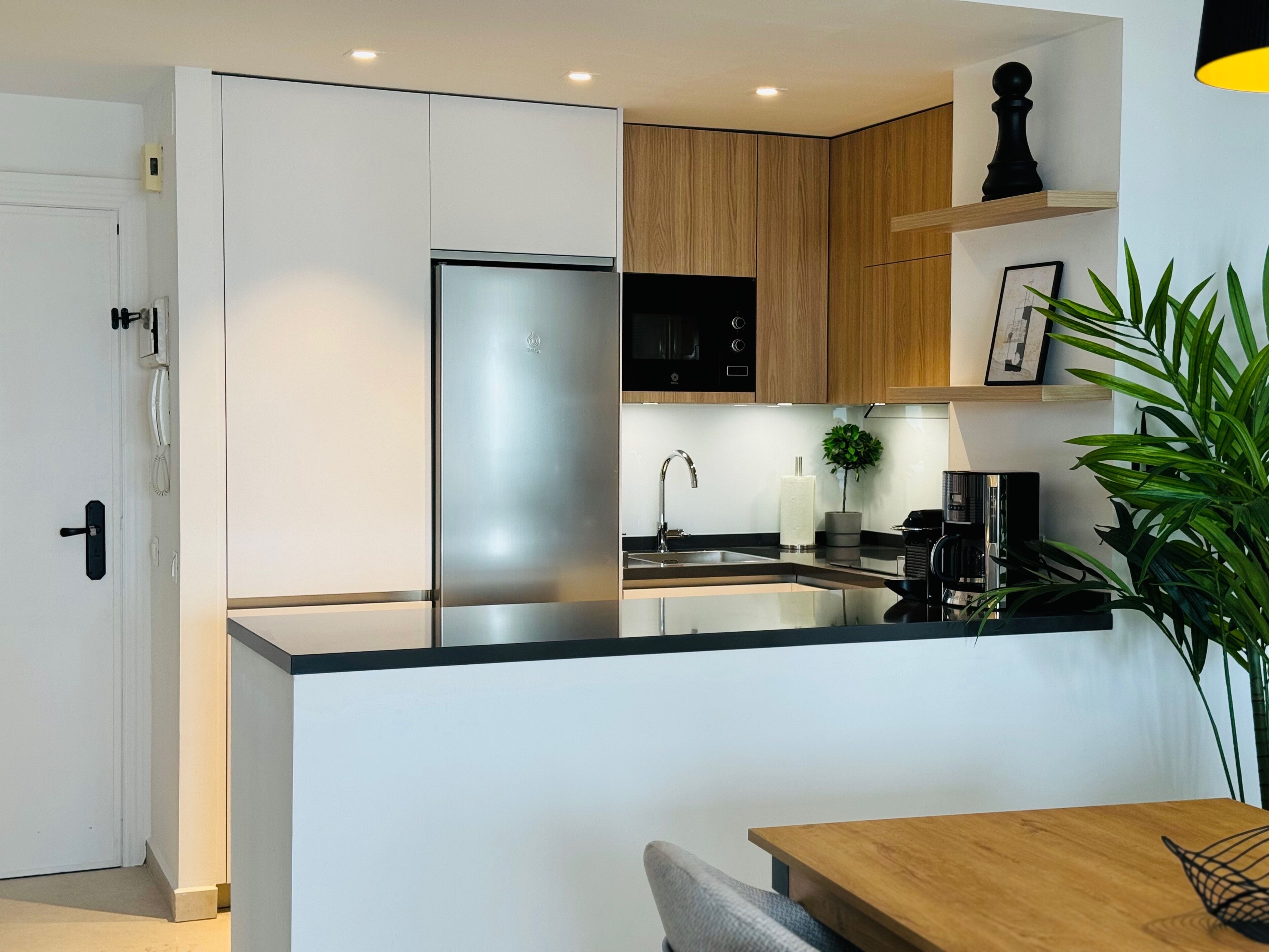 Eine moderne Küche mit weißen und hölzernen Schränken, einem Edelstahlkühlschrank, einer schwarzen Mikrowelle und einem Holzespeisetisch.
