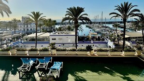Ein Yachthafen mit Booten, ein Poolbereich mit Liegestühlen und ein Gebäude mit Schildern für eine Kneipe und ein Restaurant.