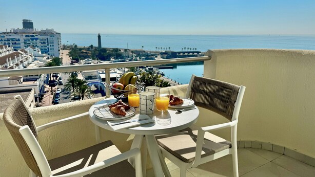 Ein Balkon mit gedecktem Tisch für das Frühstück, mit Blick auf einen Hafen und Gebäude.