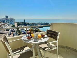 Een balkon met een ontbijt gedekte tafel, met uitzicht op een jachthaven en gebouwen.