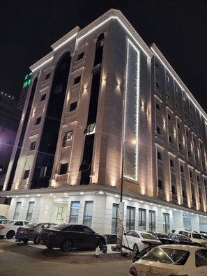 A multi-story hotel with a modern facade, illuminated windows, and a parking lot with several cars. - Qurtoba Al Aziziah (Makkah)