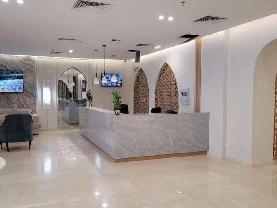 Una moderna zona de recepción con una barra de mármol, un televisor montado en la pared y un área de descanso con sofá y sillones.