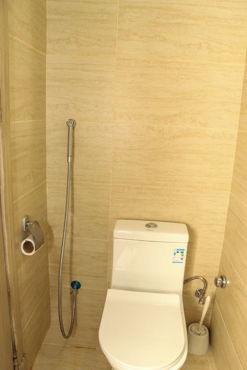 A small, enclosed bathroom with a toilet, a shower, and a toilet paper holder.