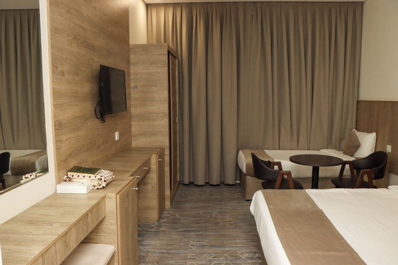A hotel room with a bed, a desk, a chair, a small table, a television, and a curtain.