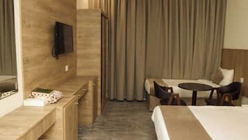 Habitación de hotel con cama, escritorio con teléfono, televisión montada en la pared y un área de descanso con mesa y sillas.