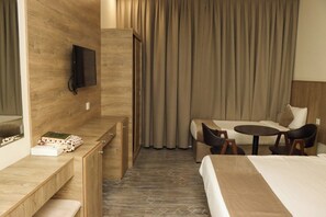 A hotel room with a bed, a desk with a telephone, a television mounted on the wall, and a seating area with a table and chairs. - Qurtoba Al Aziziah (Makkah)