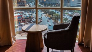 Ein Zimmer mit großem Fenster und Blick auf eine Stadtlandschaft, darunter hohe Gebäude und eine belebte Straße.