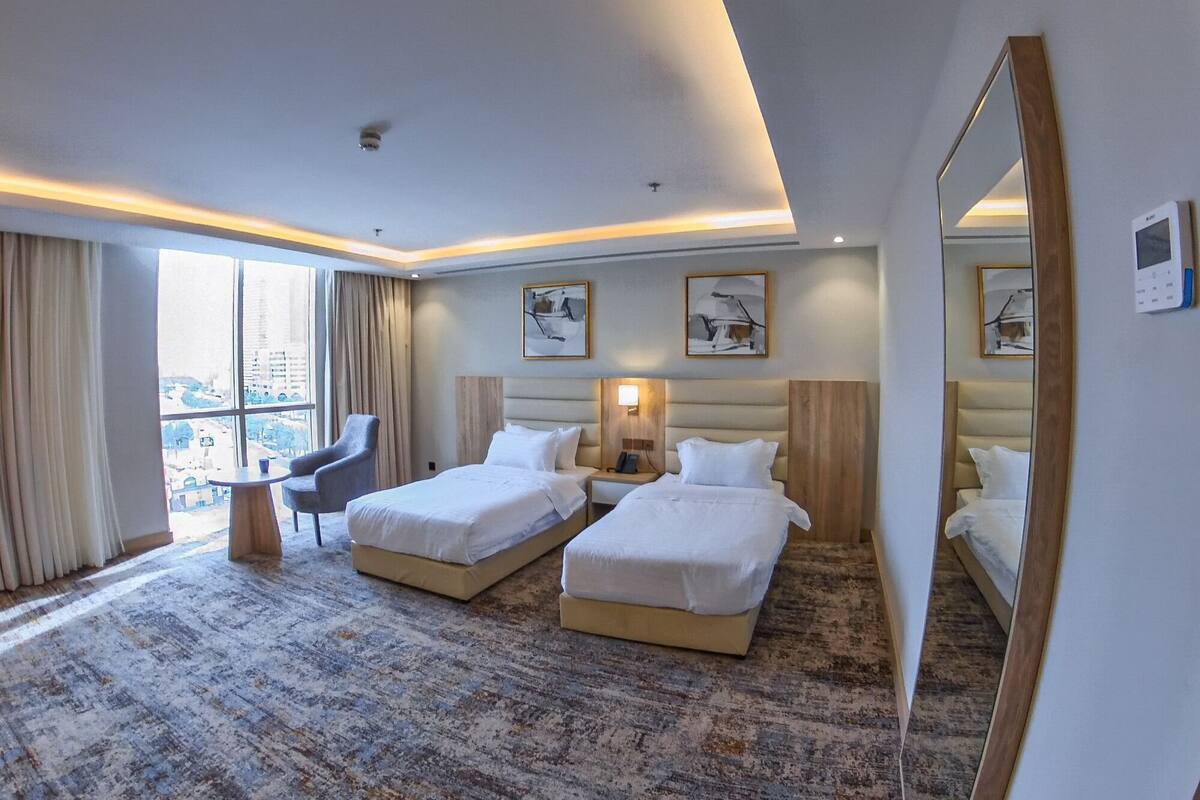 A hotel room with two beds, a desk, a chair, and a large window.