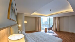 Ein Hotelzimmer mit einem großen Bett, einem Schreibtisch, einem Stuhl und Blick auf die Stadt durch große Fenster.