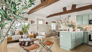 A spacious living room with a sofa, coffee table, and chairs, a kitchen with light blue cabinets, and a dining area. - Bijou • Romantic Sanctuary, Hot Tub in Boulders (Yucca Valley)