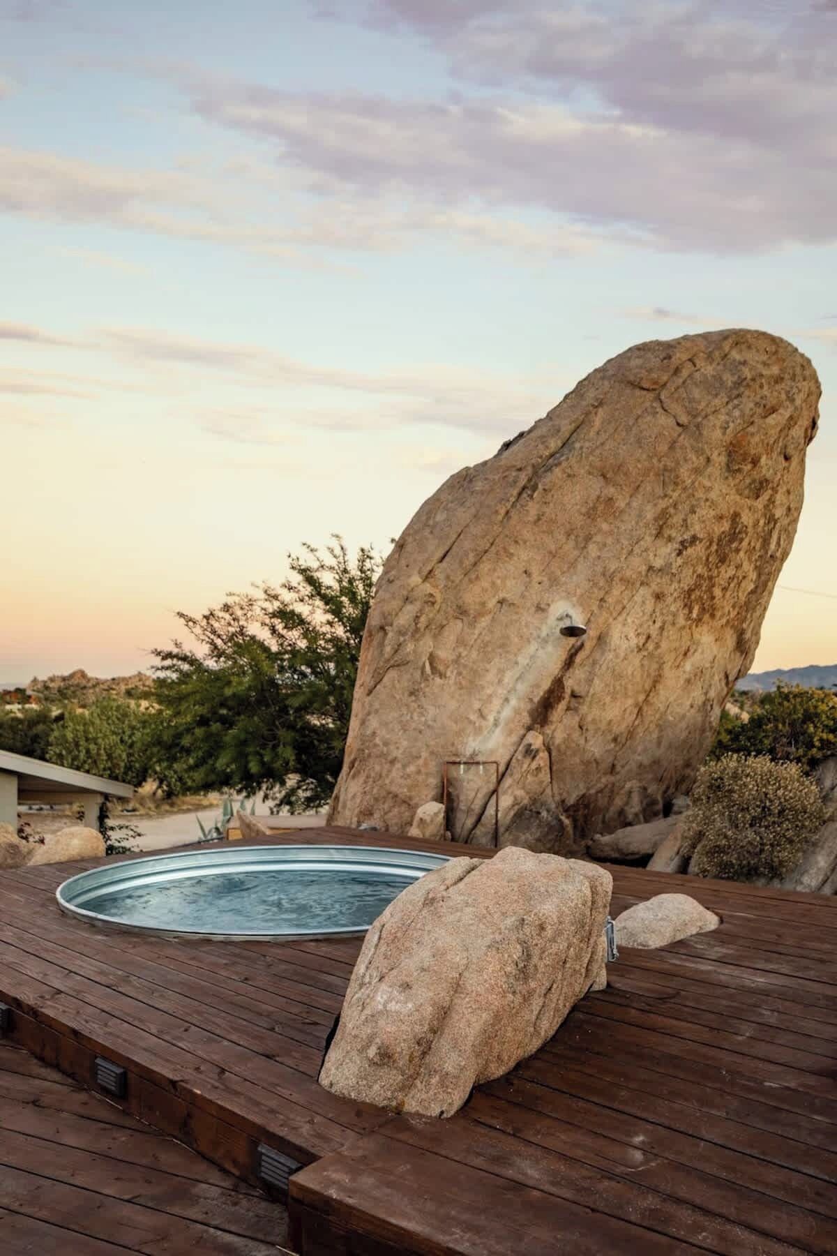 Un jacuzzi en una terraza de madera con una roca grande cerca.