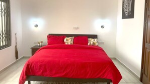 Un dormitorio con una cama grande, dos mesitas de noche, una mesita auxiliar, un cuadro de cebra colgado en la pared y una ventana con barandillas decorativas.