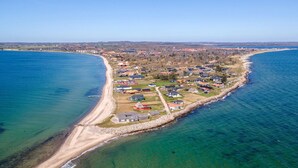 Vista aérea de una zona residencial costera con casas a lo largo de la orilla, una playa de arena y un mar azul cristalino.