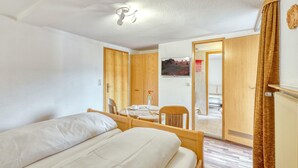A hotel room with a bed, a wooden chair, a small table with a vase of flowers, a television, and a view of the outside.