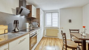 A modern kitchen with a stove, oven, and microwave. There is a dining table with chairs and a window with blinds.