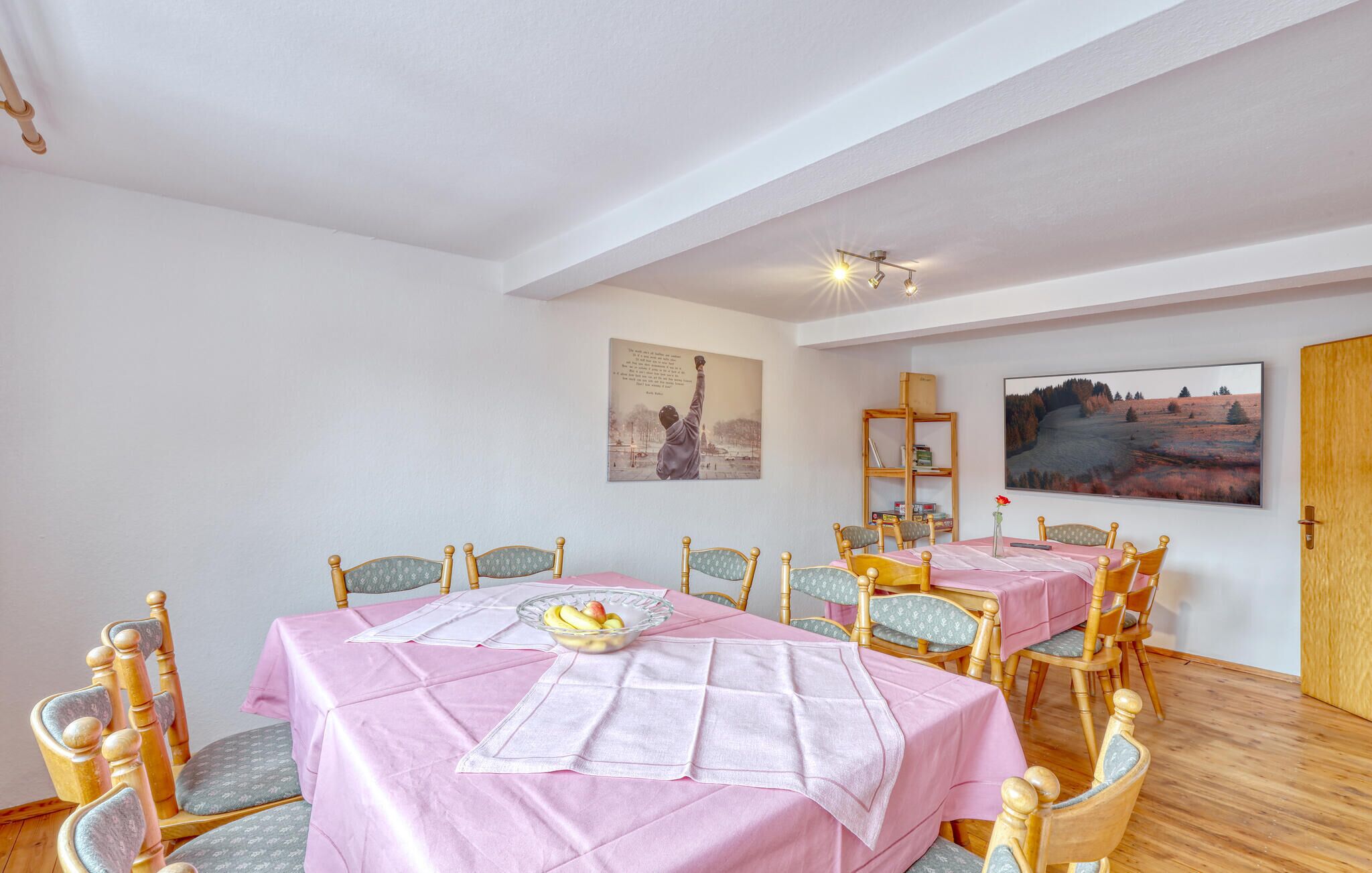A dining room with two tables covered in pink tablecloths, wooden chairs, and a fruit bowl on the table.
