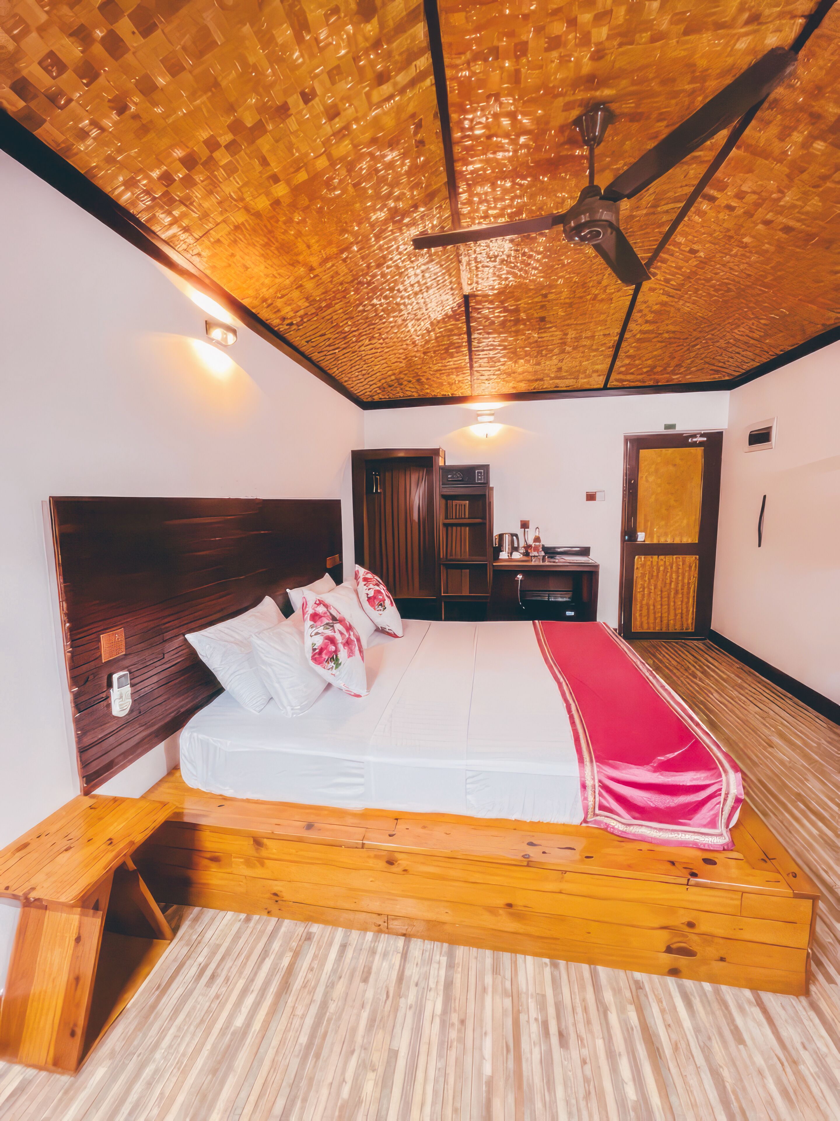 A room with a bed, wooden headboard, a ceiling fan, a wooden bench, and a small table.