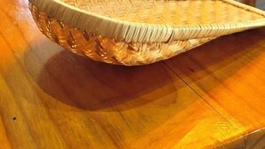 Una habitación con una mesa de madera, una cesta tejida, un sofá con cojines y una ventana que da a vistas de vegetación.