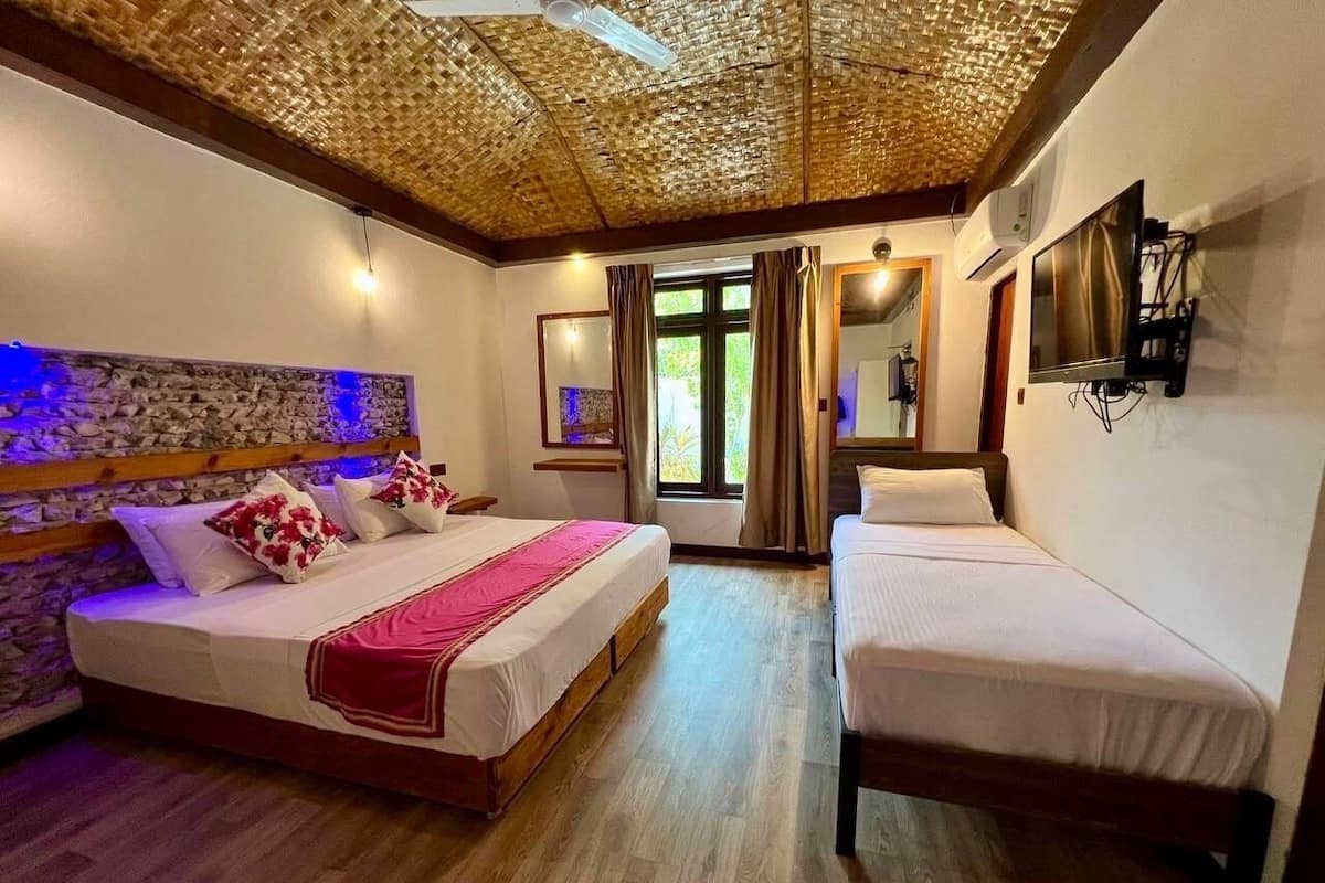 A hotel room with two beds, a stone wall, a wooden ceiling, and a TV mounted on the wall.