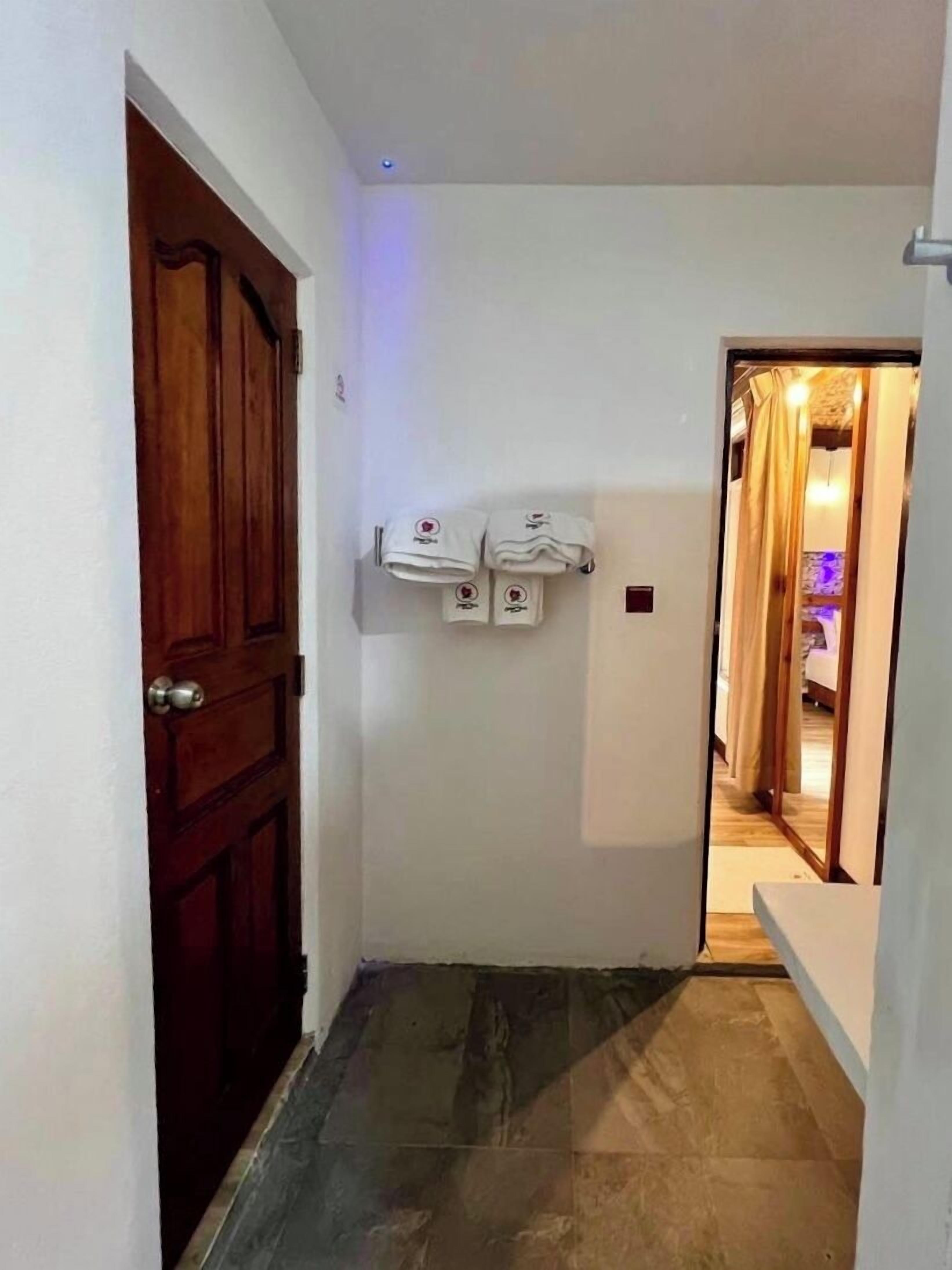 Um corredor com porta de madeira, piso de azulejo e porta-toalhas fixado na parede.