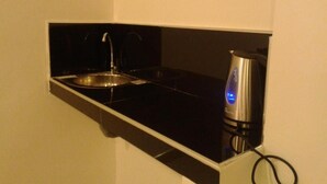 Een kleine kitchenette met een spoelbak, een waterkoker en een aanrecht.