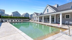 A swimming pool with a stone border, lounge chairs, and a covered patio area.