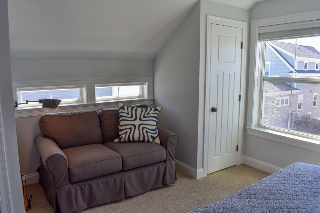 A room with a brown sofa, a patterned pillow, a door, and a window with a view of buildings.