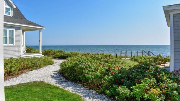 A coastal property with a gravel path leading to a wooden deck overlooking the sea.