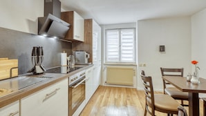 A modern kitchen with a stove, oven, and microwave. There is a dining table with chairs and a window with blinds. - Amazing apartment in Bischofsheim (Bischofsheim)