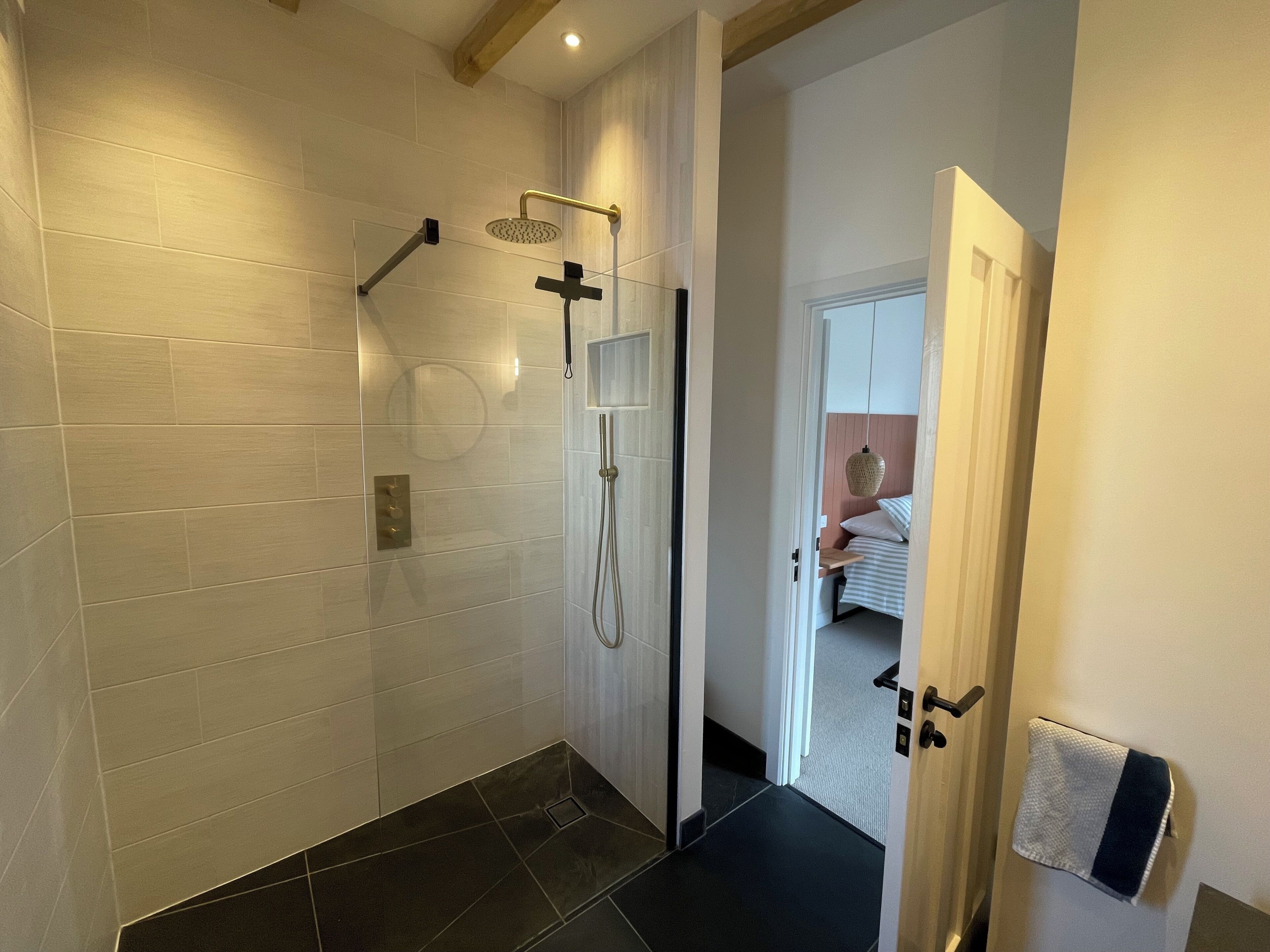 Une salle de bain moderne avec une douche à parois de verre, des murs recouverts de carreaux blancs et un sol noir.