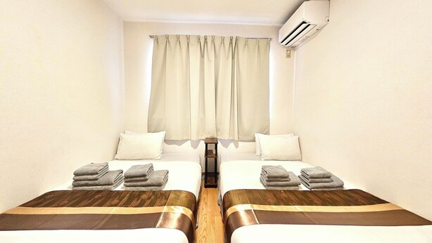 Une chambre d’hôtel avec deux lits, une fenêtre avec des rideaux, un appareil de climatisation et une petite table.