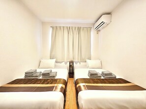 Una habitación de hotel con dos camas, una ventana con cortinas, un equipo de aire acondicionado y una mesita pequeña.