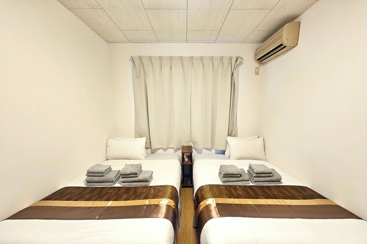 A hotel room with two beds, each with a brown headboard, white bedding, and folded towels.