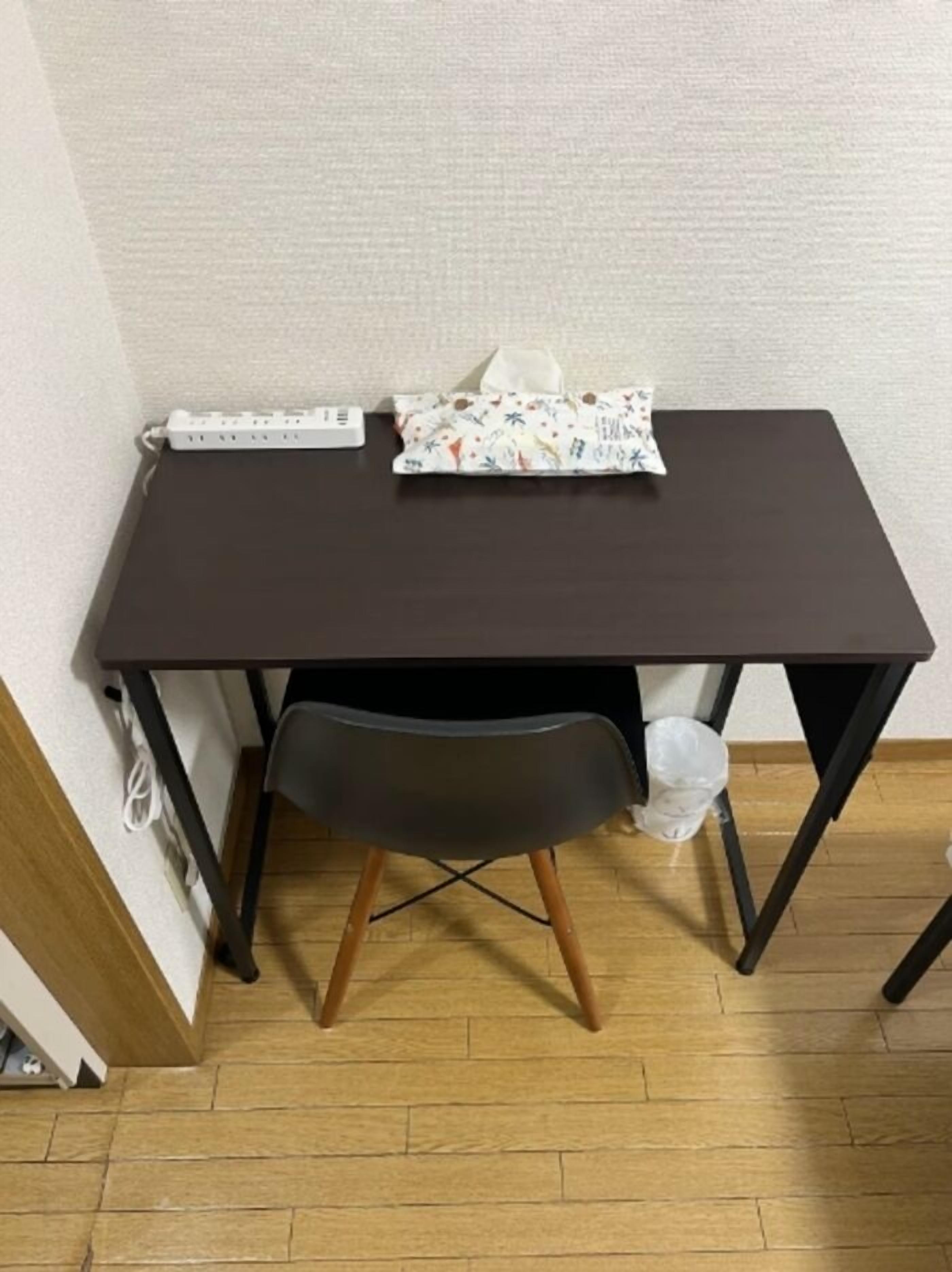 A small, dark-colored desk with a chair, a power strip, and a tissue box.