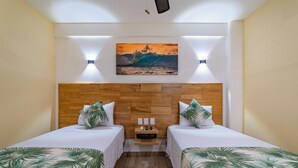 A hotel room with two beds, a wooden headboard, a painting of a wave, and a nightstand with a lamp.