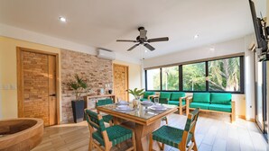 A dining area with a wooden table and chairs, a ceiling fan, and a green sofa by a large window.