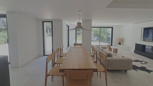 Uma sala de jantar moderna com uma mesa de madeira comprida e cadeiras, um sofá e uma televisão.