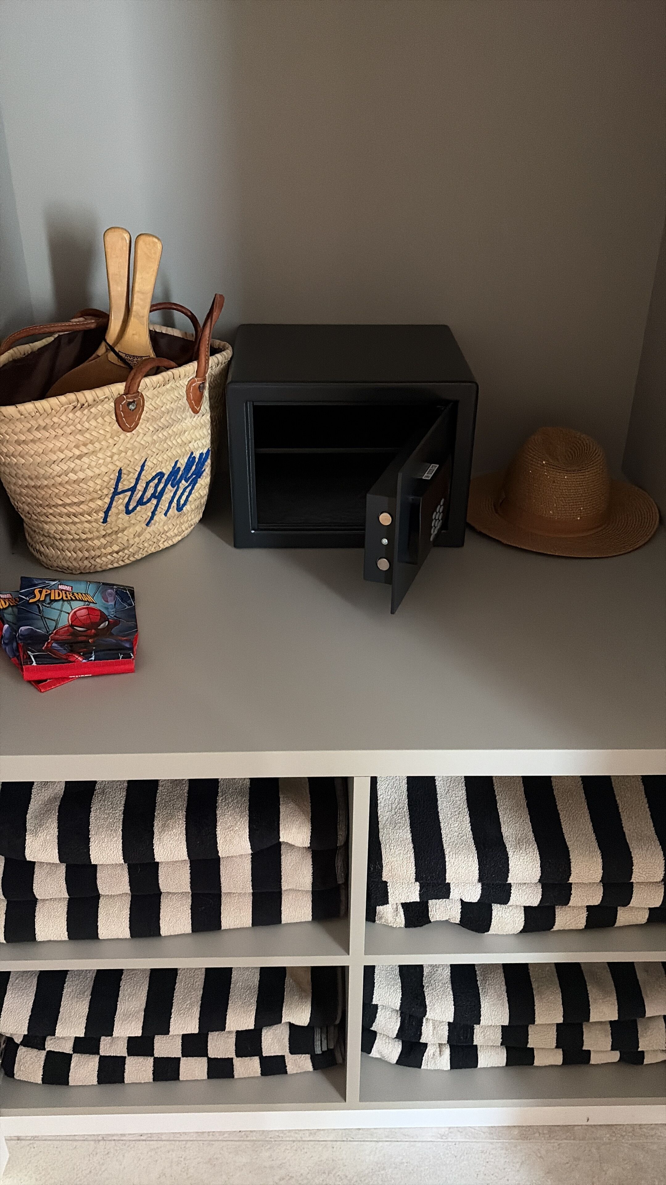 Una habitación con una cesta tejida, un mueble negro para guardar objetos, un sombrero y cojines a rayas.