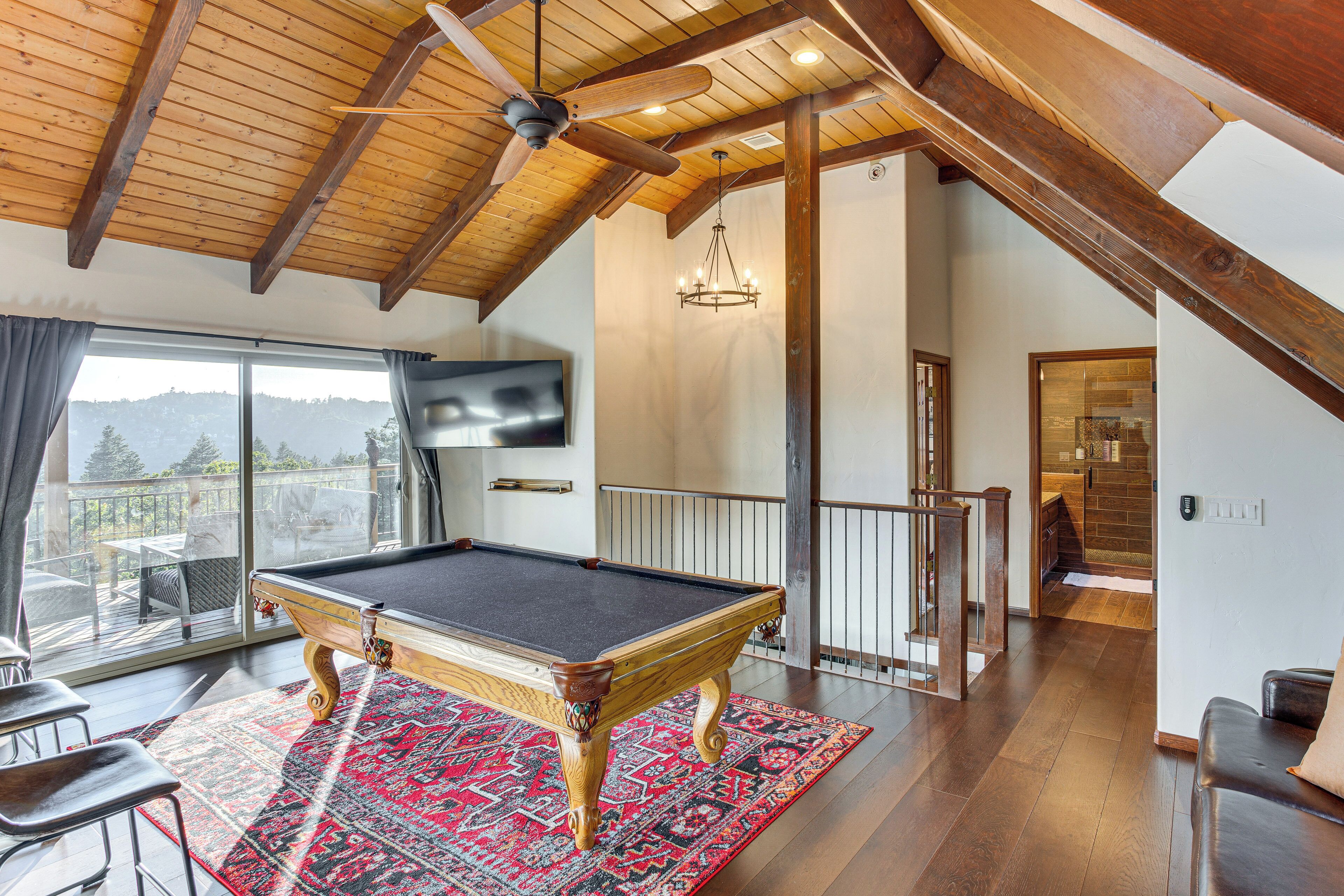 A pool table in a room with a wooden ceiling, a chandelier, and a view of the outdoors.
