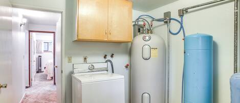 Un espace buanderie comprenant un lave-linge, un chauffe-eau et un réservoir d’eau.