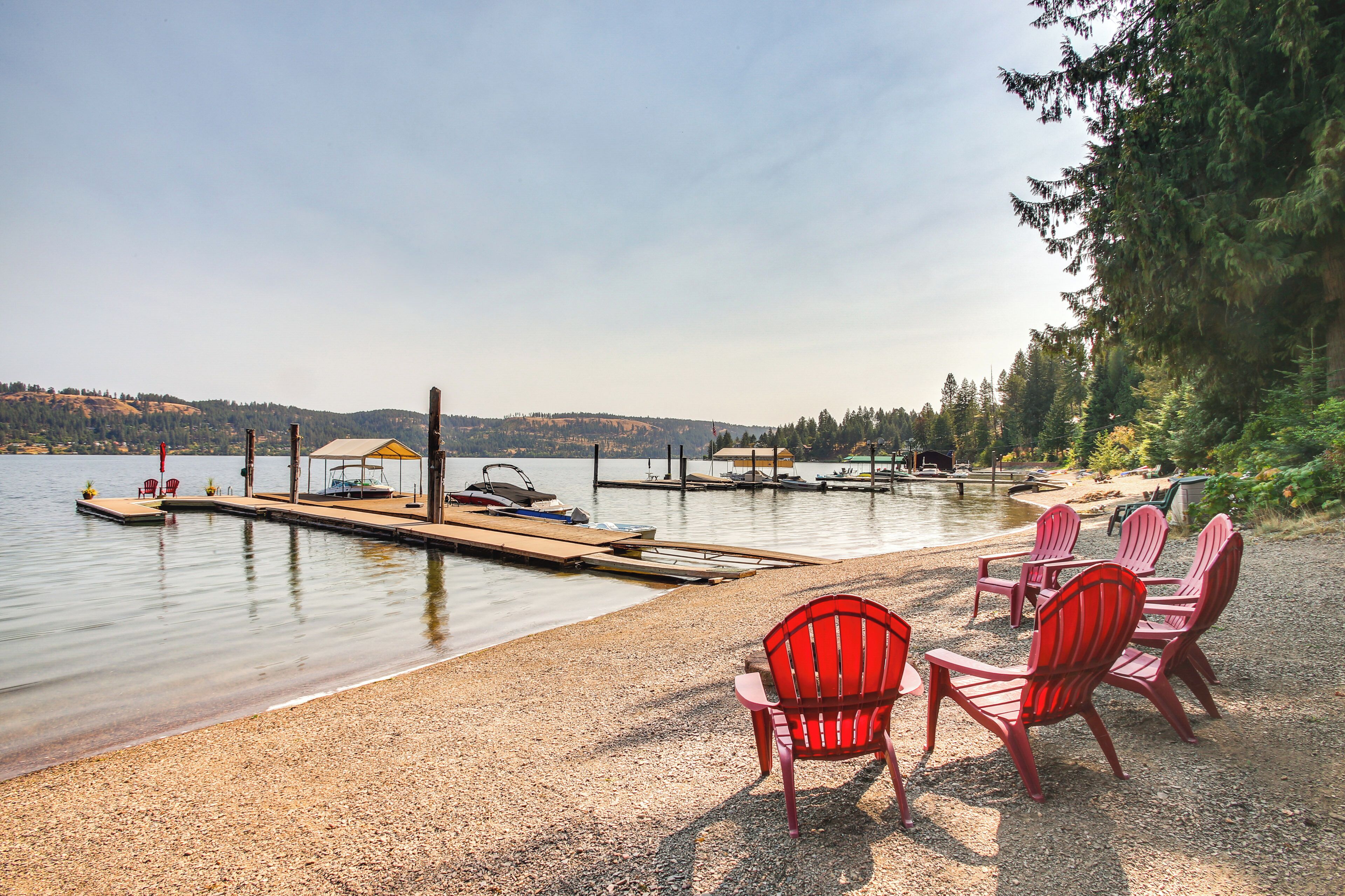 Una terrazza sul lago con poltrone Adirondack rosse, un molo con barche e un gazebo.