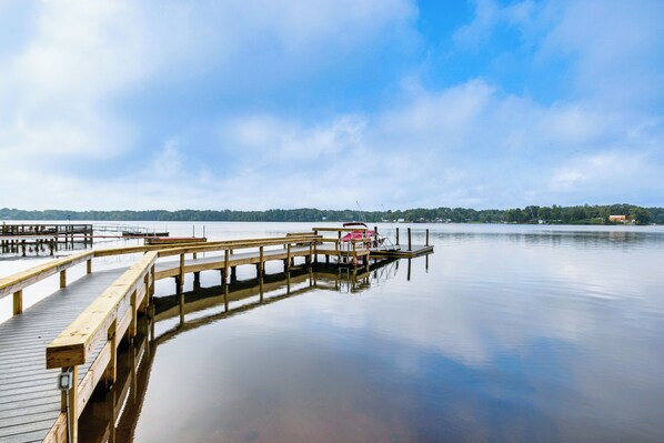 A wooden pier extending into calm water, with a docked boat and a distant shoreline with buildings. - Private Boat Dock: Waterfront Lake Murray Haven (Prosperity)