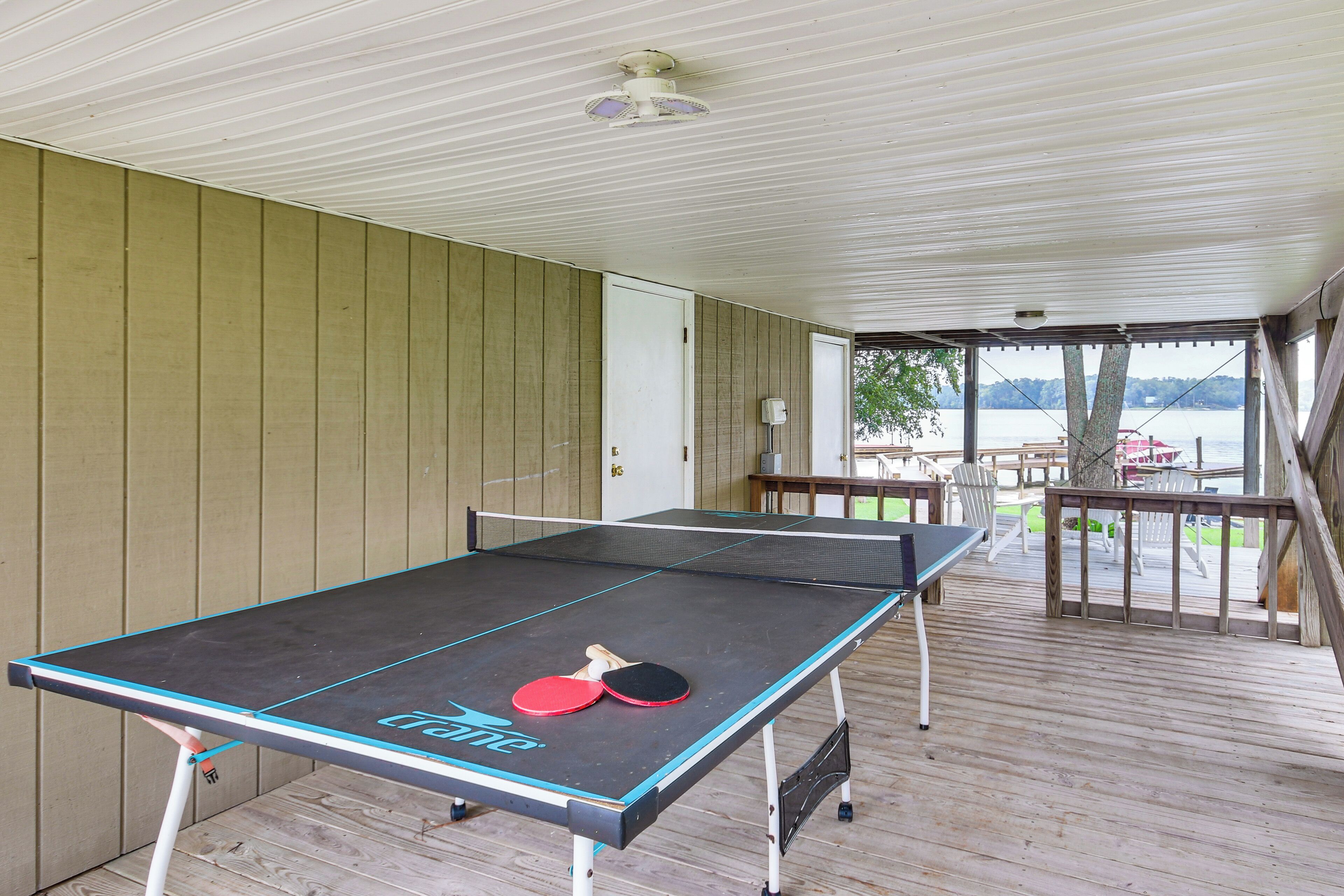 Une table de ping-pong avec deux raquettes, installée sur une terrasse en bois offrant une vue sur un lac.